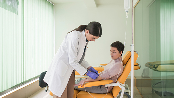 Healthcare professional preparing an IV for a patient seated in an orange recliner chair in a clinical setting.